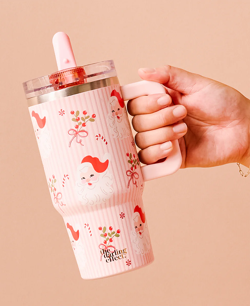 Tumbler with cartoon santa designs held by a hand against a beige background