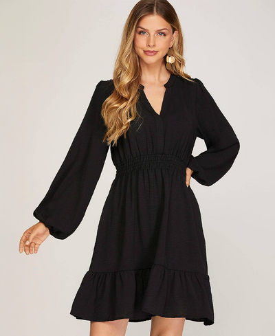 Woman wearing a black dress with long sleeves on a plain background