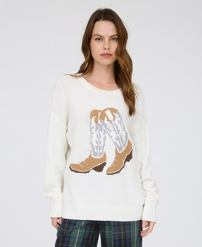 Woman wearing a cream sweater with a cowboy boot design on a plain background