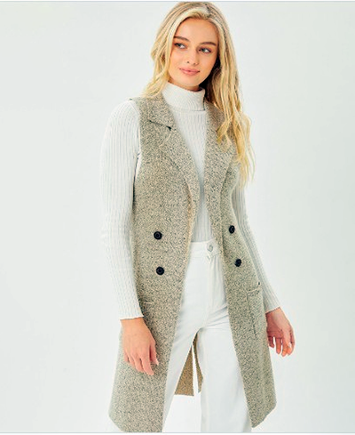 Woman wearing a long beige vest over a white sweater and pants on a light gray background