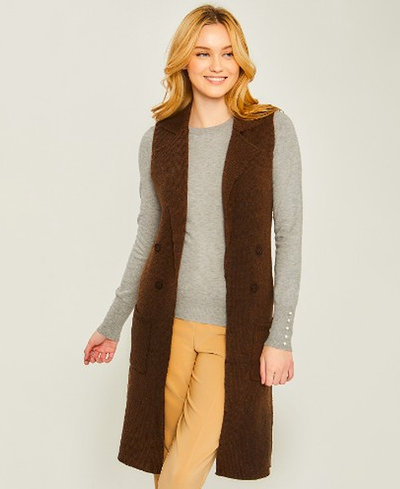 Woman wearing a brown vest over a gray sweater and beige pants on a plain background