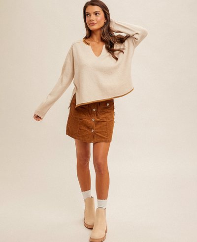Woman wearing a beige sweater and brown skirt on a plain background