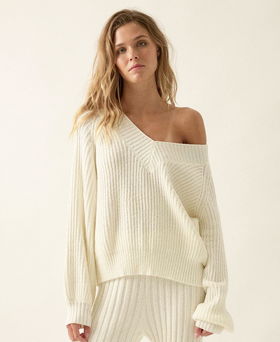 Woman wearing a white off-shoulder sweater against a plain background