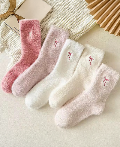 Set of four pairs of soft socks in pink and white on a textured surface.
