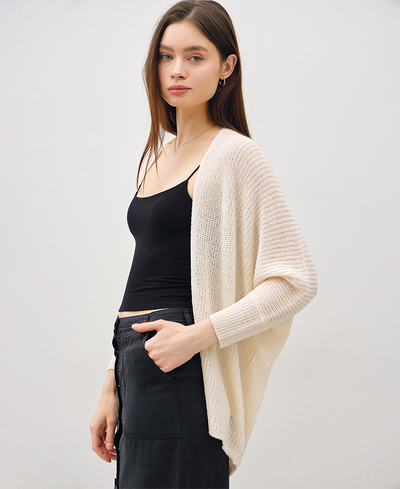 Woman wearing an ivory cardigan over a black top and pants on a white background
