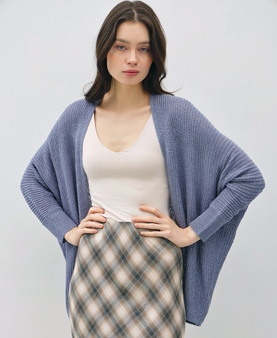 Woman wearing a blue cardigan over a white top and plaid skirt on a light gray background