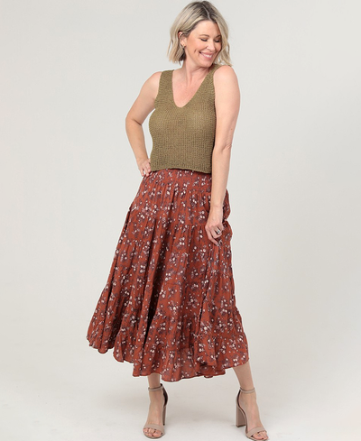 Woman wearing a green top and rust-colored floral skirt on a white background