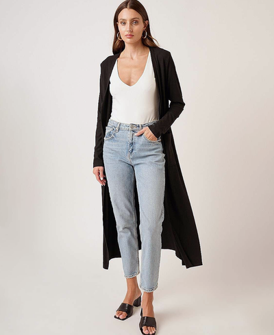 Woman wearing a long black cardigan, white top, and light blue jeans on a plain background