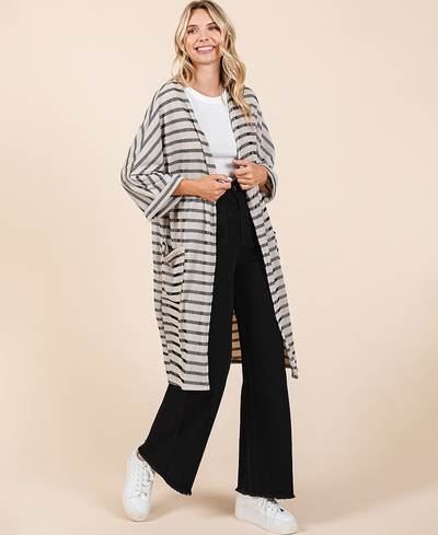 Woman wearing a striped cardigan, white shirt, black pants, and white sneakers on a beige background