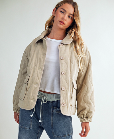 Woman wearing a beige jacket over a white shirt and blue jeans on a plain background