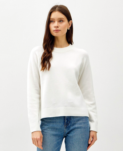 Woman wearing a white sweater and blue jeans on a light gray background