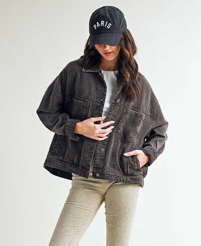 Person wearing a dark denim jacket, light gray shirt, beige pants, and a black cap with 'PARIS' text on a white background.