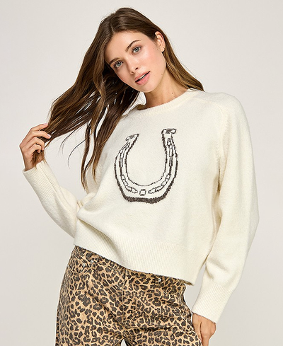 Woman wearing a cream sweater with a horse shoe design and leopard print pants on a light background