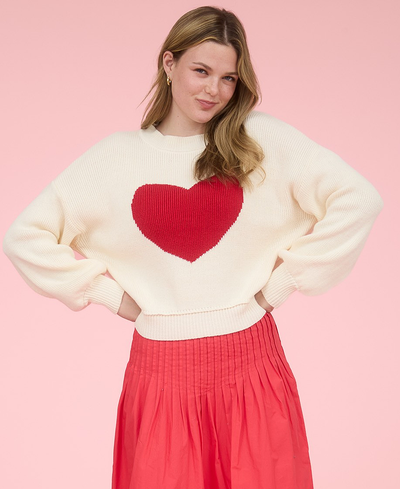 Woman wearing a cream sweater with a red heart design against a pink background