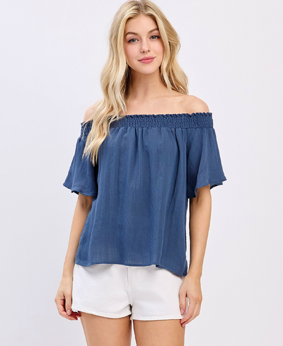 Woman wearing a blue off-shoulder top and white shorts on a light gray background