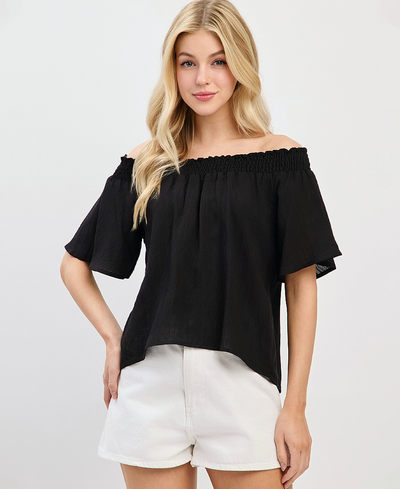 Woman wearing a black off-shoulder top and white shorts on a light gray background