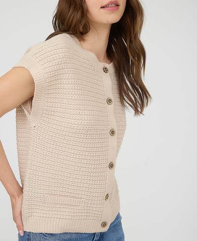 Woman wearing a beige knitted vest with button details on a plain background