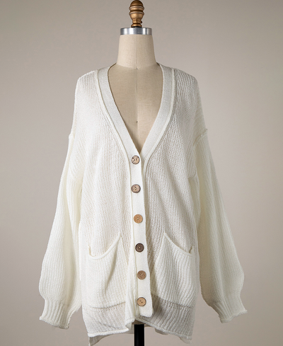 White cardigan with brown buttons on a mannequin against a beige background