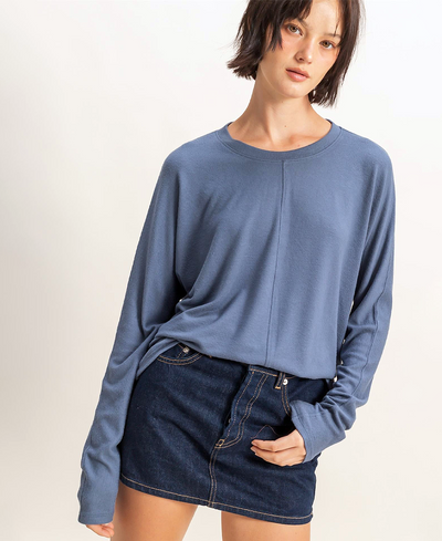 Woman wearing a blue long-sleeve top and denim skirt on a plain background