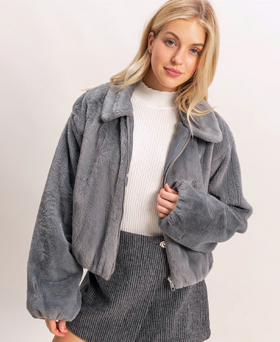 Woman wearing a gray jacket over a white sweater on a plain background