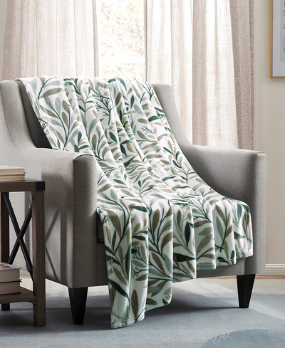 Green leaf-patterned blanket draped over a gray armchair in a living room setting.