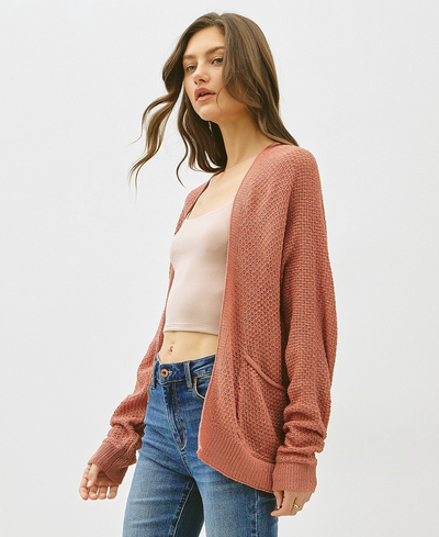 Woman wearing a clay cardigan over a beige top and blue jeans on a white background