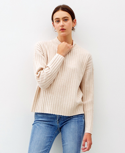 Woman wearing a beige ribbed sweater and blue jeans against a white background