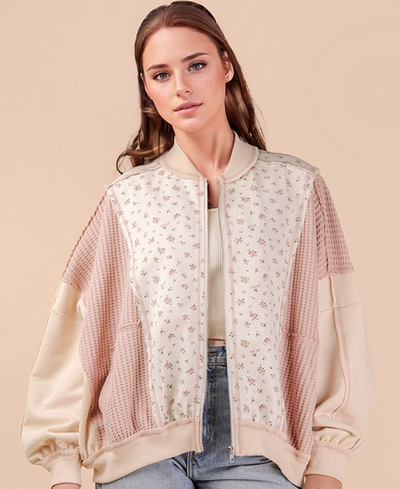 Woman wearing a light pink bomber jacket with floral pattern on a beige background