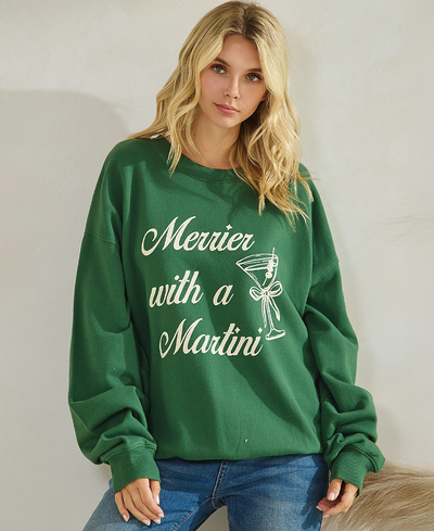 Woman wearing a green sweatshirt with 'Merrier with a Martini' text and martini graphic.