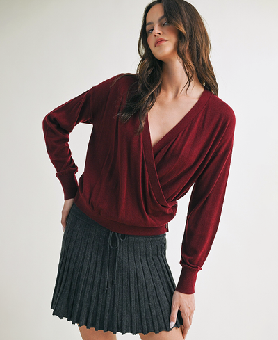 Woman wearing a burgundy long-sleeve top and black pleated skirt on a white background