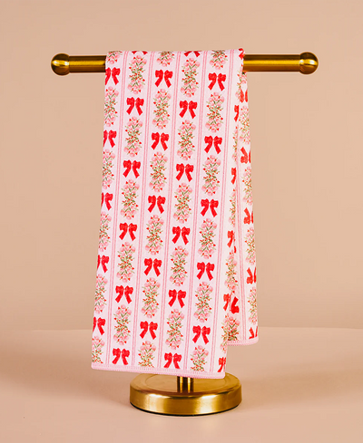 Decorative towel with red bow pattern on a gold towel rack against a beige background