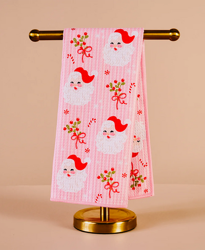 Pink towel with Santa Claus design on a gold towel rack against a beige background