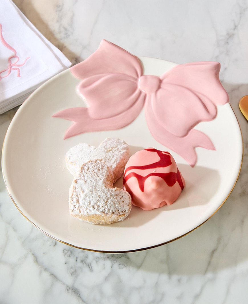 Two heart-shaped pastries on a plate with a pink bow decoration on a marble surface.