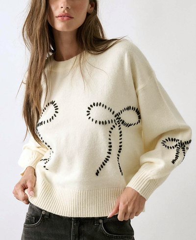 Woman wearing a cream sweater with black bow designs on a white background