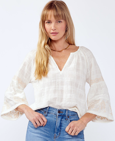 Woman wearing a white blouse with sheer sleeves and blue jeans on a white background