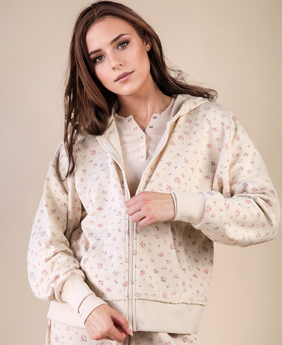 Woman wearing a cream-colored hoodie with a subtle floral pattern on a beige background