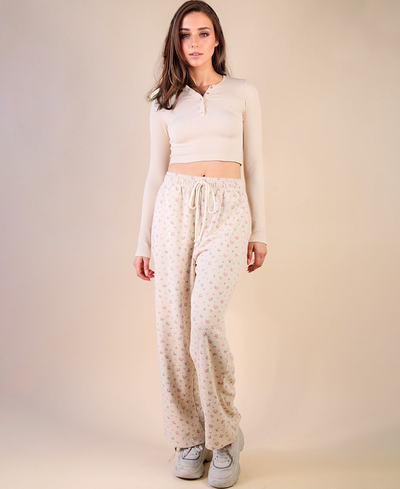 Woman wearing a cream-colored outfit with floral patterned joggers against a beige background