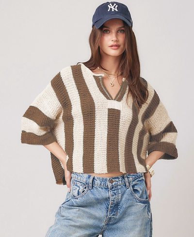 Person wearing a brown striped sweater and blue jeans with a cap on a light background