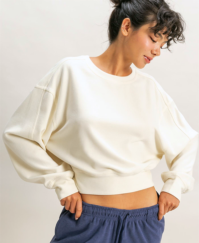 Person wearing a cream sweatshirt and blue pants against a plain background