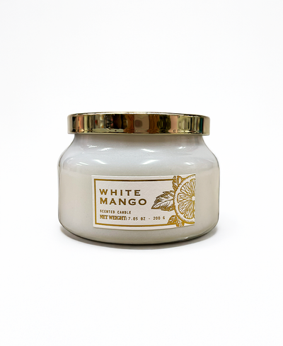 White mango scented candle with gold lid and label on a white background