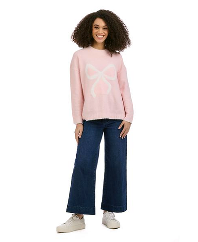 Woman wearing a pink sweater with a bow design and blue jeans on a white background